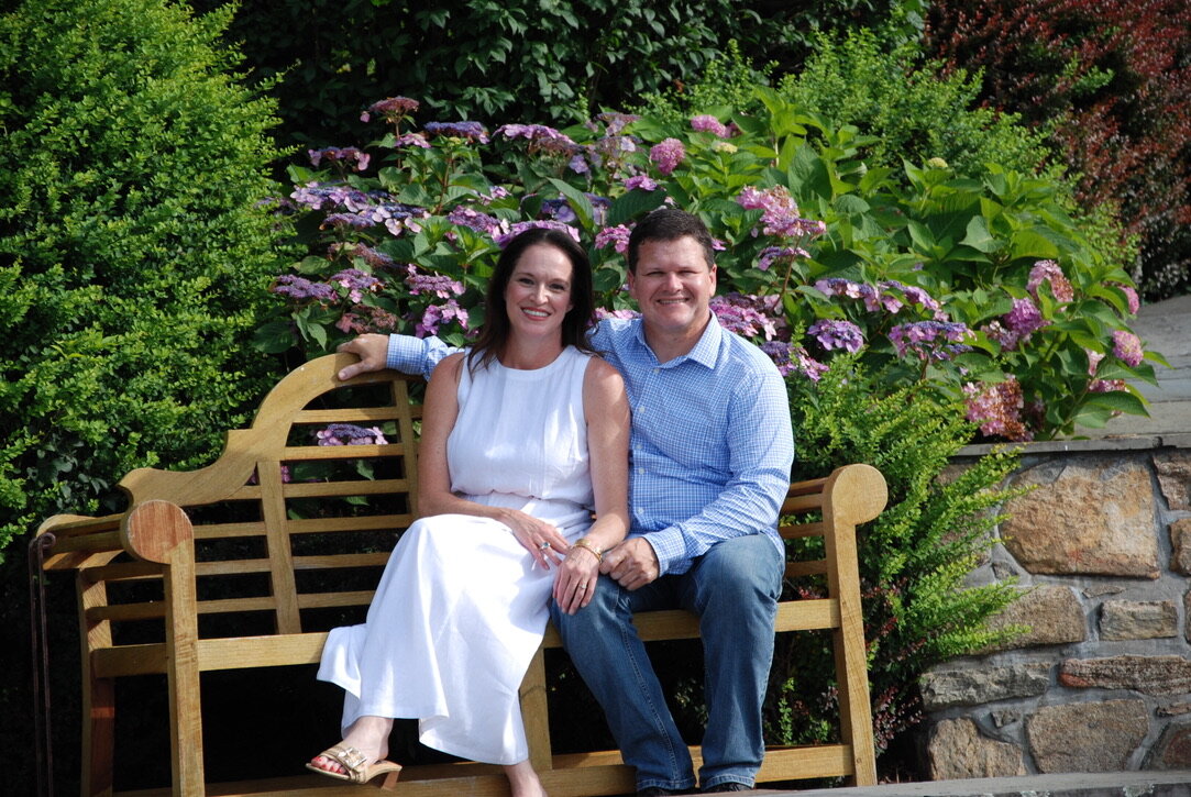 Julie and Jay seated on a wooden bench with hydrangeas